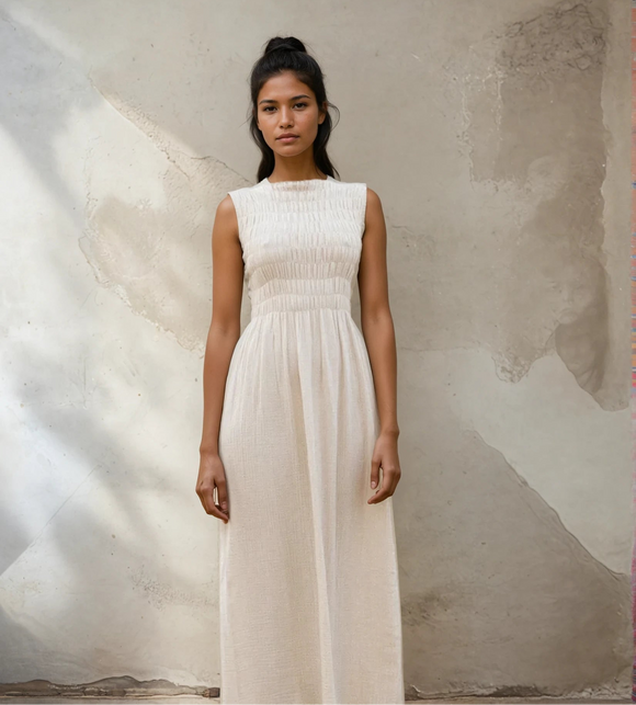 Woman wearing a sand colour dress standing against a textured wall.