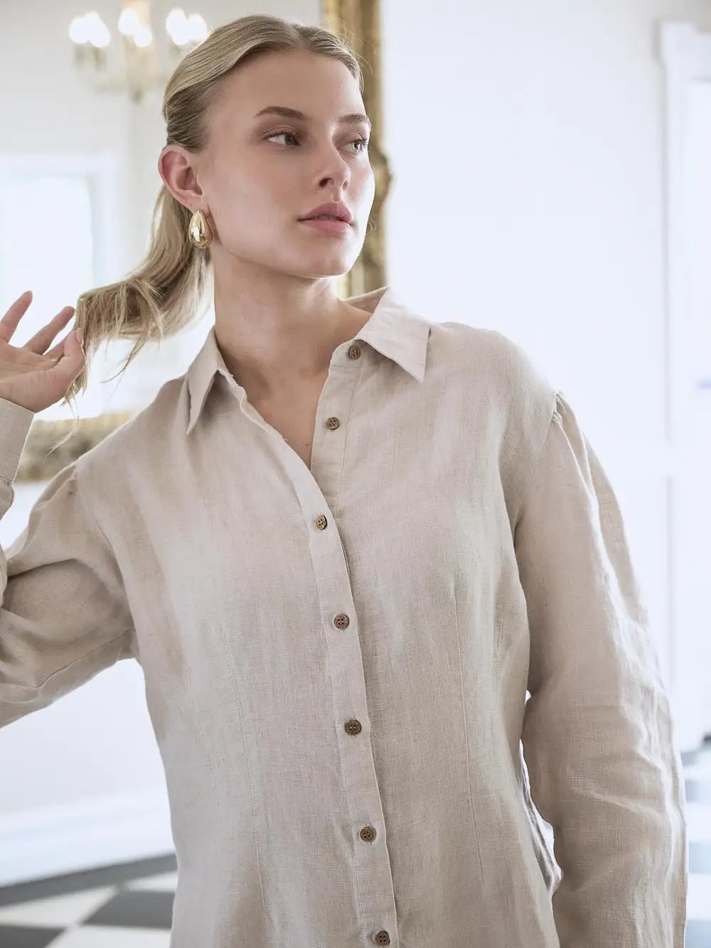 Woman wearing a beige button-up shirt in an indoor setting