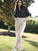 Woman wearing a black blouse and beige pants standing outdoors with trees and grass in the background