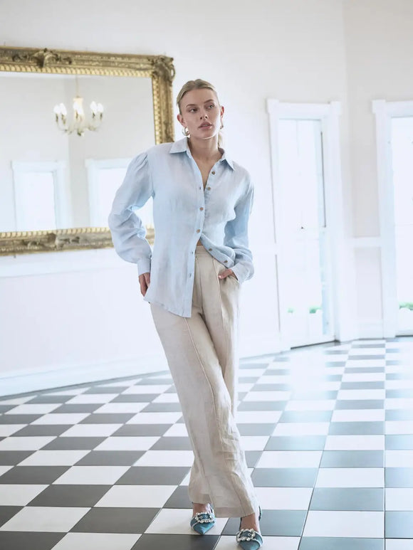Person wearing a light blue shirt and beige pants in a room with checkered floor and large mirror.
