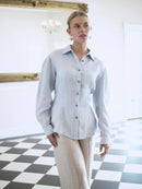 Woman wearing a light blue shirt and beige pants in an indoor setting with a checkered floor.